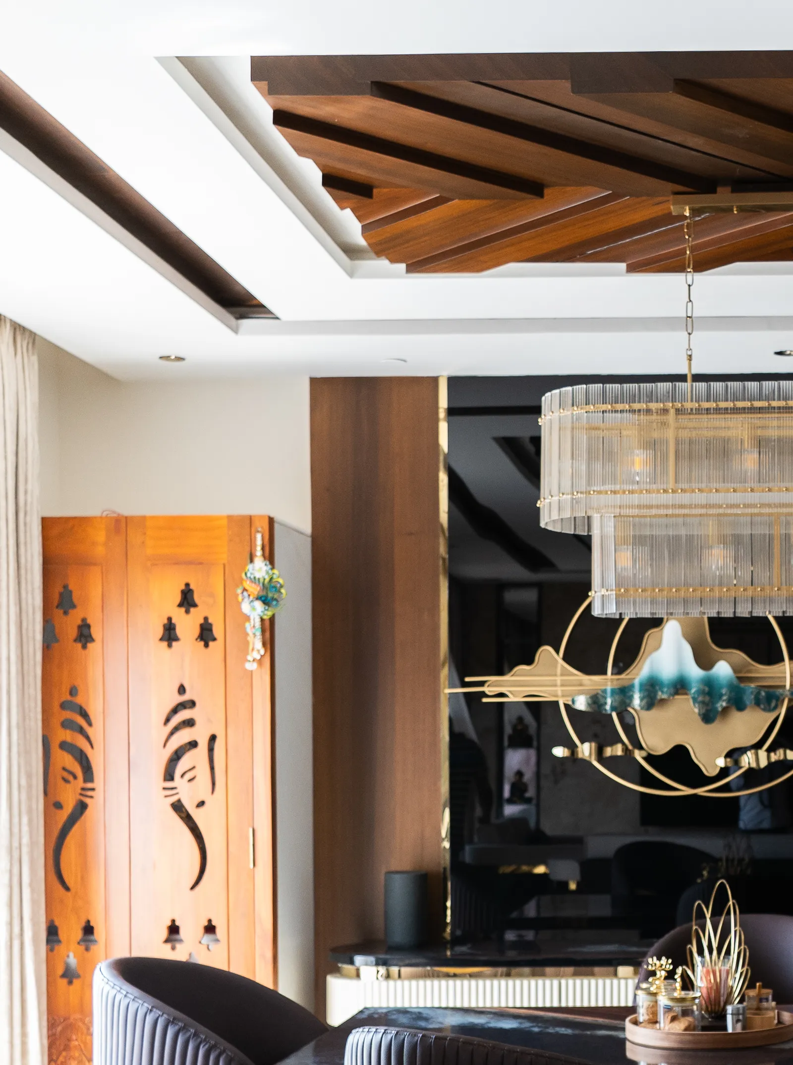 Dining area with crystal chandelier, sculptural wall art and carved wooden door — Abhishek's Residence